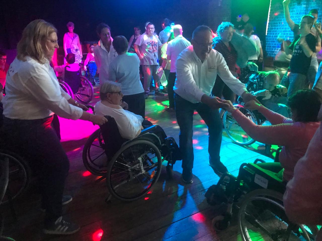Gasten en vrijwilligers dansen samen, met en zonder rolstoel.