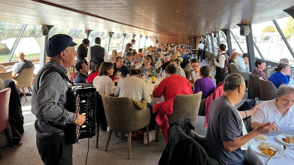 Een accordeonist speelt terwijl een grote groep samen eet op een boot.