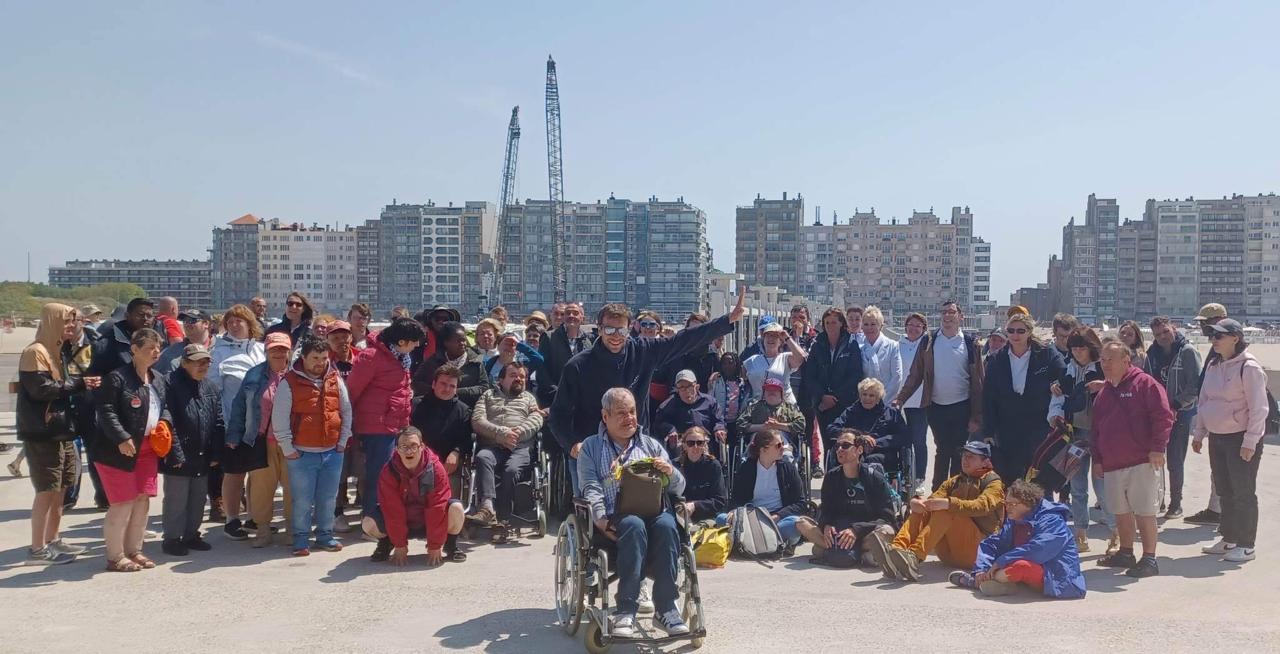 De groep poseert bij de zee, met appartementsgebouwen op de achtergrond.