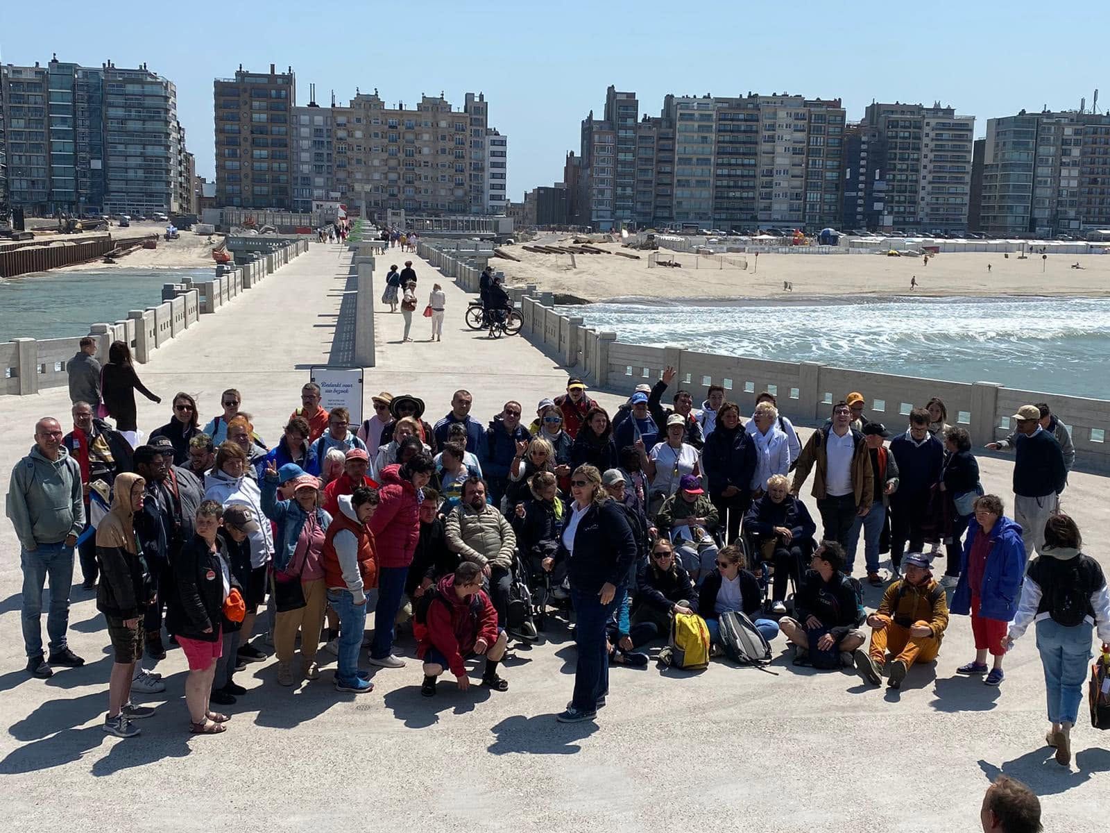 De groep poseert op een strand, voor een dijk en appartementsgebouwen.